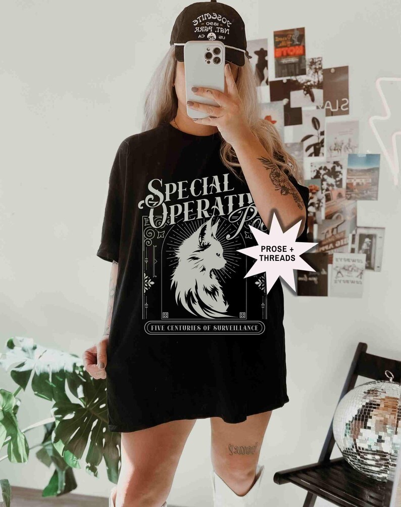 May include: Black t-shirt with a white graphic of a fox and the words "SPECIAL OPERATIONS" and "FIVE CENTURIES OF SURVEILLANCE". The shirt is paired with a black baseball cap.
