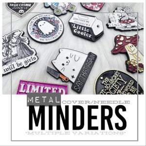 May include: A collection of metal pin minders with various designs, including a ghost, a cat with a knife, and text that reads "Say That Again." The pins are in various colors and shapes, with the word "LIMITED" visible on one.