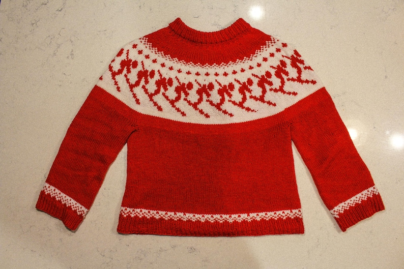 Puede incluir: Un jersey rojo tejido con un patr&oacute;n blanco alrededor del canes&uacute; y los pu&ntilde;os. El patr&oacute;n blanco presenta figuras estilizadas. El jersey tiene cuello redondo y mangas largas. El dobladillo inferior y los pu&ntilde;os tienen un borde decorativo blanco.