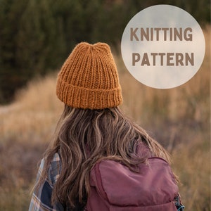 Könnte beinhalten: Eine Person trägt eine braune Strickmütze und ein kariertes Hemd und steht mit einem Rucksack auf dem Rücken auf einem Feld. Der Text "Knitting Pattern" ist in einem weißen Kreis im Hintergrund sichtbar.