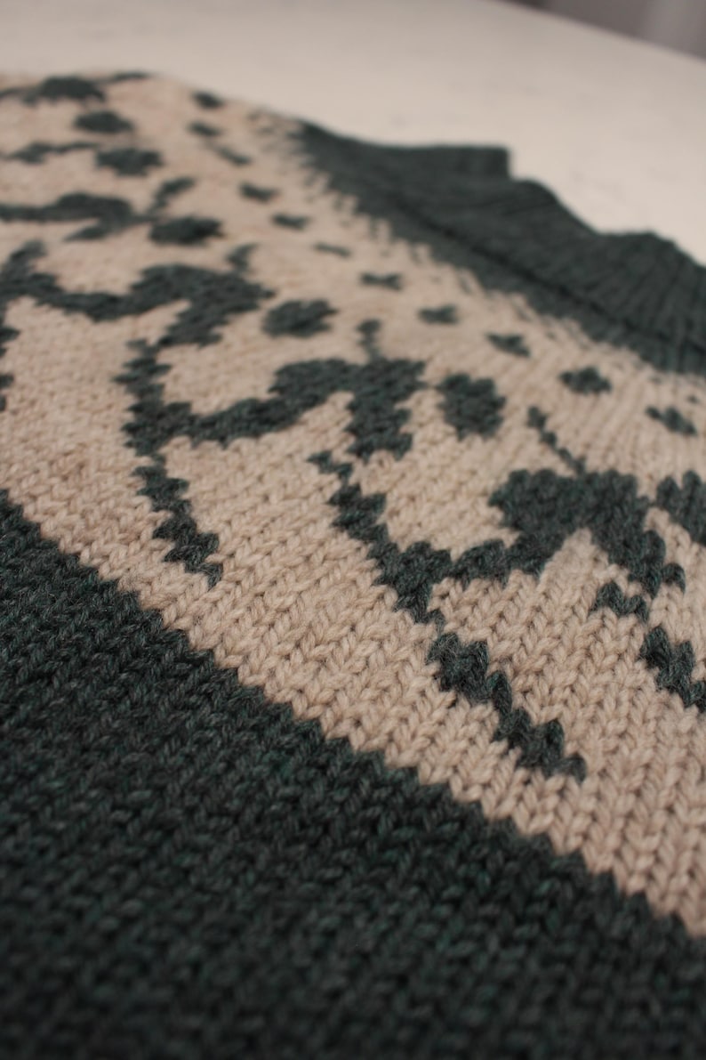 Puede incluir: Primer plano de una tela de punto con un patr&oacute;n repetitivo. El dise&ntilde;o presenta formas verde oscuro sobre un fondo beige. Los bordes y el escote son de color verde oscuro liso. La textura del tejido es visible.