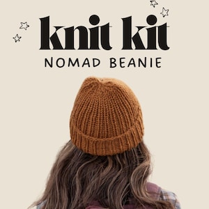 May include: A brown ribbed knit beanie worn on the head, positioned below the text "knit kit" and "NOMAD BEANIE" with small star illustrations on a light beige background. The beanie features a thick folded brim and vertical knit texture.