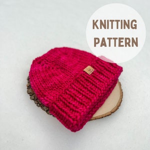 May include: A bright pink knitted beanie hat with a small brown leather label. The hat is sitting on a wooden slice. The text "KNITTING PATTERN" is written in brown text on a white circle.