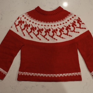 Puede incluir: Jersey de punto rojo con un estampado blanco con tem&aacute;tica de esqu&iacute; en el pecho y los pu&ntilde;os. El jersey tiene cuello redondo y mangas largas. El dise&ntilde;o incluye esquiadores en acci&oacute;n, creando un look invernal festivo.