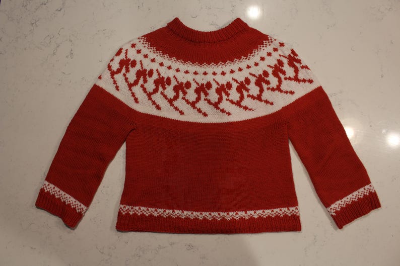 Puede incluir: Jersey de punto rojo con un estampado blanco con tem&aacute;tica de esqu&iacute; en el pecho y los pu&ntilde;os. El jersey tiene cuello redondo y mangas largas. El dise&ntilde;o incluye esquiadores en acci&oacute;n, creando un look invernal festivo.