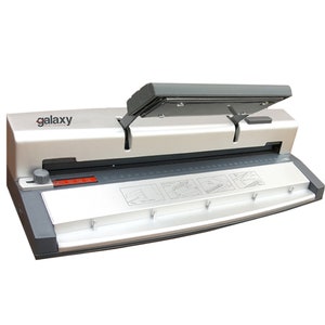 May include: A silver and black Galaxy brand electric paper punch with a lever on the top. The punch has a ruler and instructions for use on the front.