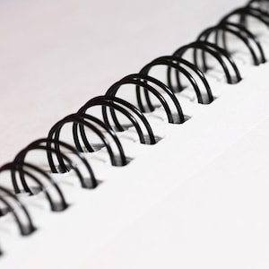 Peut inclure: Gros plan sur une reliure spirale en métal noir sur un carnet blanc.