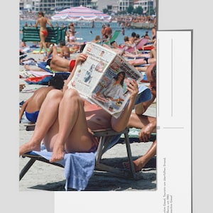Peut inclure: Une femme portant un haut de bikini et une serviette bleue est assise sur une chaise de plage en train de lire un journal tabloïd allemand appelé "Bild" avec le titre "Die Sterne stehen gut" (Les étoiles sont bonnes).