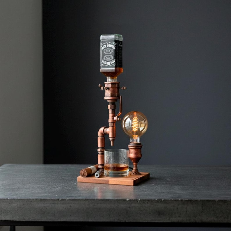 May include: A copper-toned liquor dispenser with a vintage Edison bulb and a glass of whiskey. The dispenser holds a bottle of Jack Daniel's whiskey and sits on a wooden base. A cigar rests on the base.