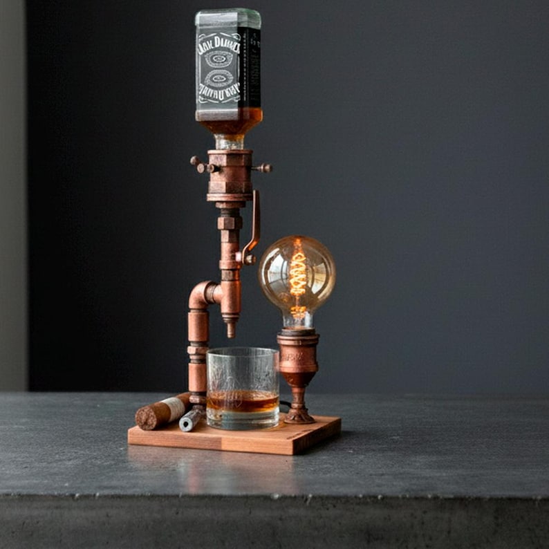 May include: A copper-toned whiskey dispenser with a vintage industrial design. It features a Jack Daniel's bottle, a glass of whiskey, a light bulb, and a wooden base. A cigar and a cigar cutter are also present.