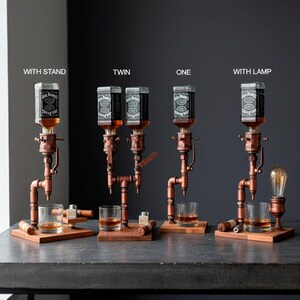 May include: A collection of copper and wood liquor dispensers, each holding a Jack Daniel's bottle. The dispensers are mounted on wooden bases, with glasses and accessories. One dispenser includes a vintage-style light bulb.