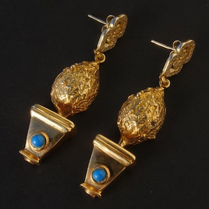 Könnte beinhalten: Goldfarbene Ohrhänger mit einem blauen Stein und einem strukturierten, blattartigen Design.