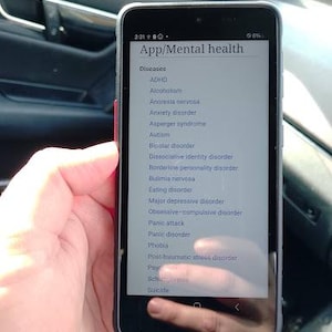 May include: A black smartphone displaying a list titled App/Mental health with a sub-heading for Diseases. The screen shows a vertical list of various mental health conditions including ADHD, Alcoholism, Anorexia nervosa, Anxiety disorder, and others.