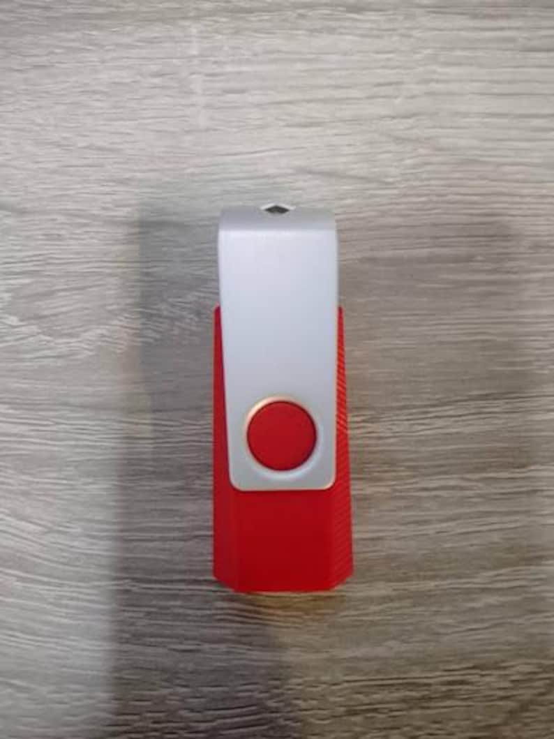 May include: A rectangular USB flash drive featuring a bright red plastic body with a textured side grip and a silver-colored metal swivel cover. The center of the silver cover displays a circular red button-like accent, and the top edge is angled.