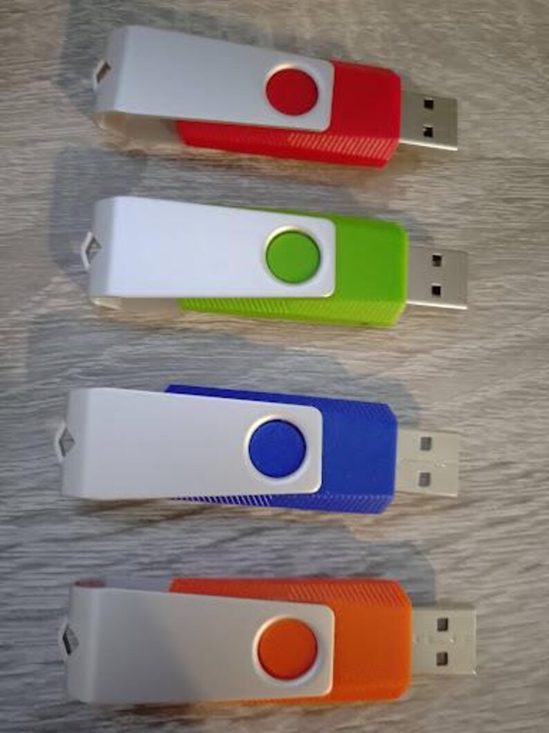 Puede incluir: Cuatro memorias USB en rojo, verde, azul y naranja. Cada unidad tiene una cubierta blanca con un bot&oacute;n de color y un conector USB. Las unidades est&aacute;n dispuestas verticalmente sobre una superficie de vetas de madera clara.