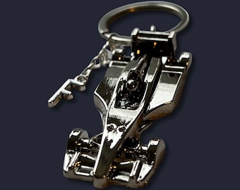 Peut inclure: Un porte-clés argenté en forme de voiture de course de Formule 1. Le porte-clés présente une réplique miniature détaillée d'une voiture de course, avec des roues, un cockpit et la lettre "F". Le porte-clés est attaché à un anneau argenté.