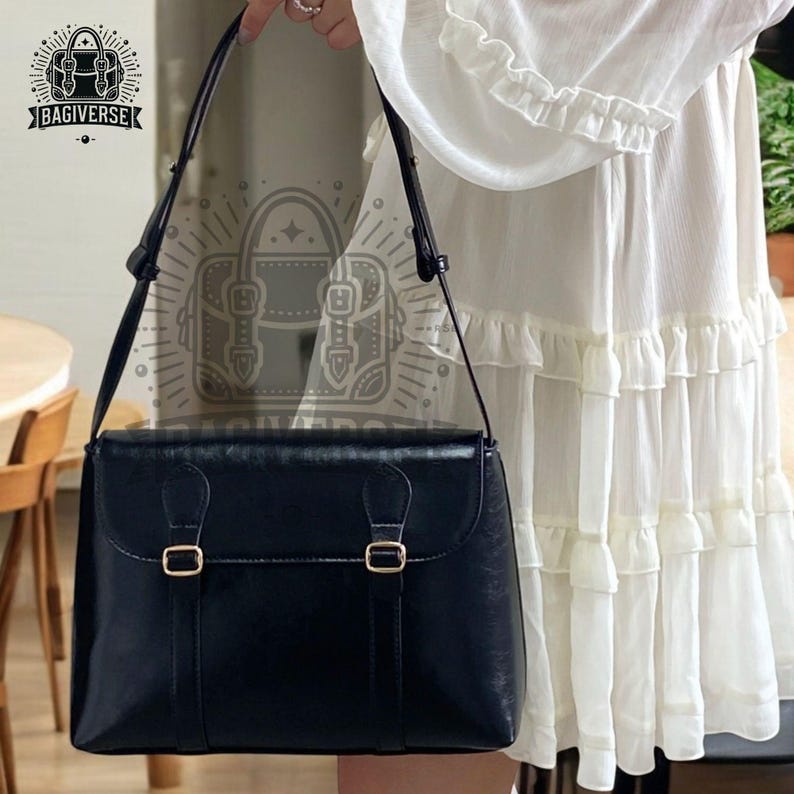 May include: A black leather satchel bag with a long shoulder strap and two gold buckles. The bag has a flap closure and a structured shape.