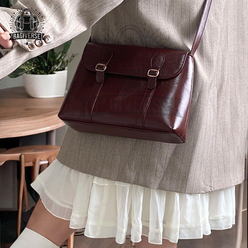 May include: A brown leather satchel bag with a flap closure and two buckles. The bag is worn over the shoulder and has a long strap.