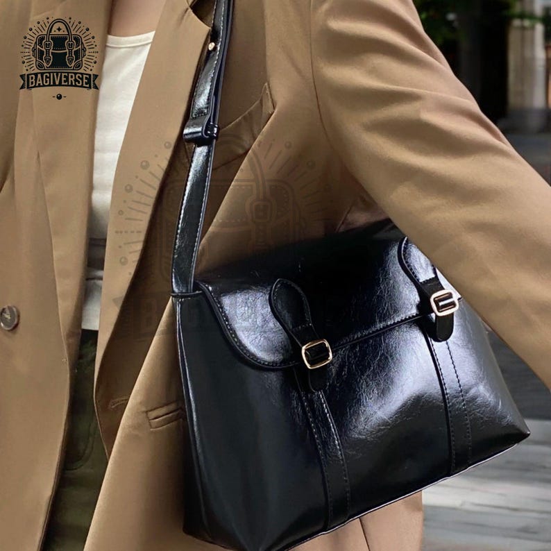 May include: A black leather shoulder bag with gold buckles and a long adjustable strap. The bag has a flap closure and a shiny finish.