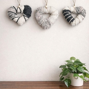 Peut inclure: Trois décorations murales en forme de cœur, faites de fil texturé blanc, gris et noir. Chaque cœur est doté d'une boucle de suspension et d'une petite perle en bois. Les cœurs sont suspendus sur un mur blanc.