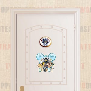 May include: A white door with a blue and gold round sticker with the text "The Opposite Attract" and an anchor symbol. Below the sticker is a blue and white Mickey Mouse ear sticker with the text "Your Name Here" and "Disney Wonder 2023" and a cartoon image of Mickey Mouse, Minnie Mouse, and Pluto. The text "Alaska" is below the image.