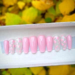 May include: A set of ten pink and white press-on nails with a cow print design. The nails are in a white box.