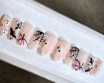 May include: A set of ten pink and white Halloween-themed press-on nails with various designs including ghosts, bats, spiders, and pumpkins.