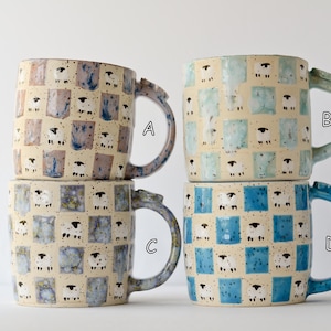 May include: Four ceramic mugs with sheep pattern. Each mug has a cream-colored base with a grid of squares, each containing a sheep illustration. The mugs have different colored handles: blue, green, and gray.