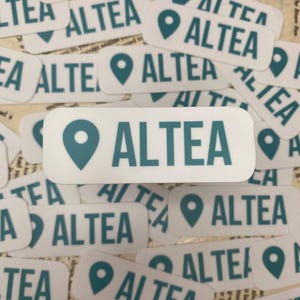 May include: A close-up of several white rectangular stickers with a teal blue location pin and the word "ALTEA" printed in teal blue.