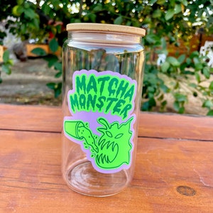 May include: A clear glass jar with a bamboo lid and a green and purple sticker that says "MATCHA MONSTER" with a green monster graphic.