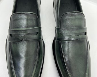 May include: A pair of dark green leather loafers with a simple design. The loafers have a rounded toe and a single strap across the vamp.