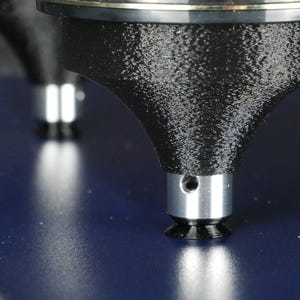 Pode incluir: Close-up de um componente de máquina preto texturizado com uma base prateada e um pequeno orifício. O componente está posicionado sobre uma superfície azul escura. Um segundo componente é visível no fundo.