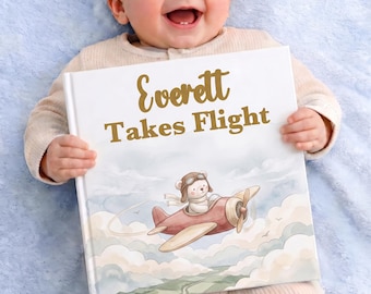 May include: A square hardcover book titled Everett Takes Flight in gold lettering. The cover features a watercolor illustration of a white bear wearing an aviator hat and goggles, piloting a small red airplane through light blue and white clouds.