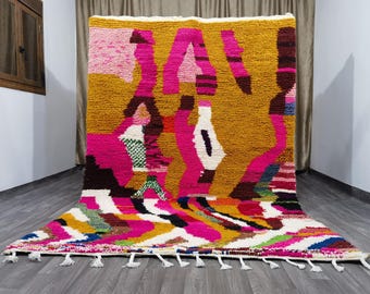 Könnte beinhalten: Ein bunter marokkanischer Teppich mit einem geometrischen Muster in den Farben Pink, Gelb, Weiß und Schwarz. Der Teppich hat einen Fransenrand.
