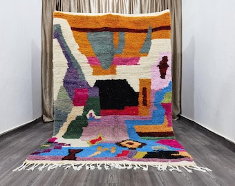 May include: A colorful abstract rug with a white background and a variety of shapes and colors, including orange, blue, green, pink, and purple. The rug has a fringe border.