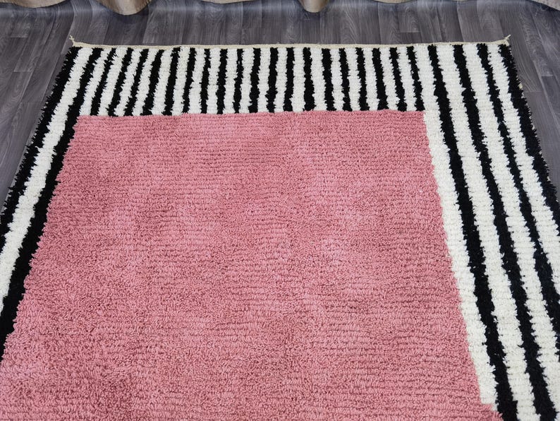 May include: A rectangular rug with a soft, textured pink center. The rug is bordered by a thick band of black and white vertical stripes. The rug is designed for home decor.