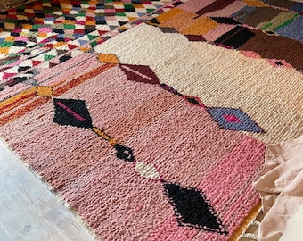 Könnte beinhalten: Ein bunter marokkanischer Teppich mit einem geometrischen Muster in den Farben Rosa, Orange, Gelb, Blau, Grün und Schwarz. Der Teppich hat einen Fransenrand und ist aus Wolle gefertigt.