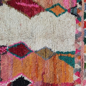 May include: A colorful Moroccan rug with a white center and geometric patterns in shades of red, pink, orange, green, and black.