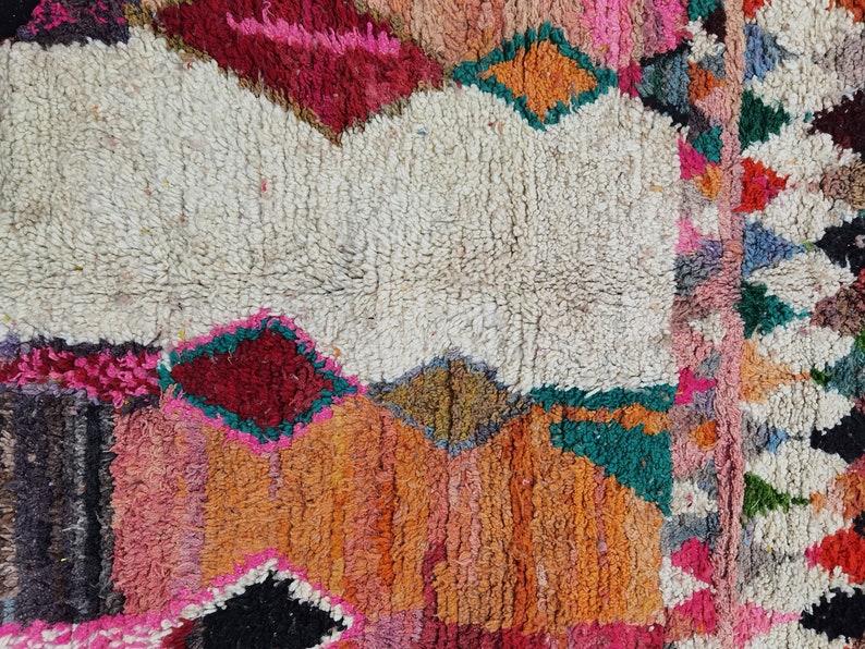 May include: A colorful Moroccan rug with a white center and geometric patterns in shades of red, pink, orange, green, and black.