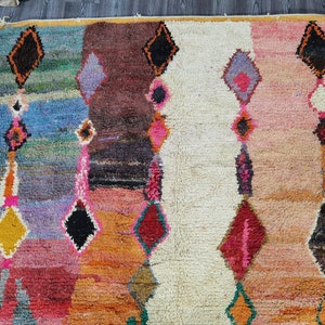 May include: A colorful Moroccan rug with a geometric pattern in shades of pink, orange, blue, and green. The rug has a white center section with a diamond pattern.