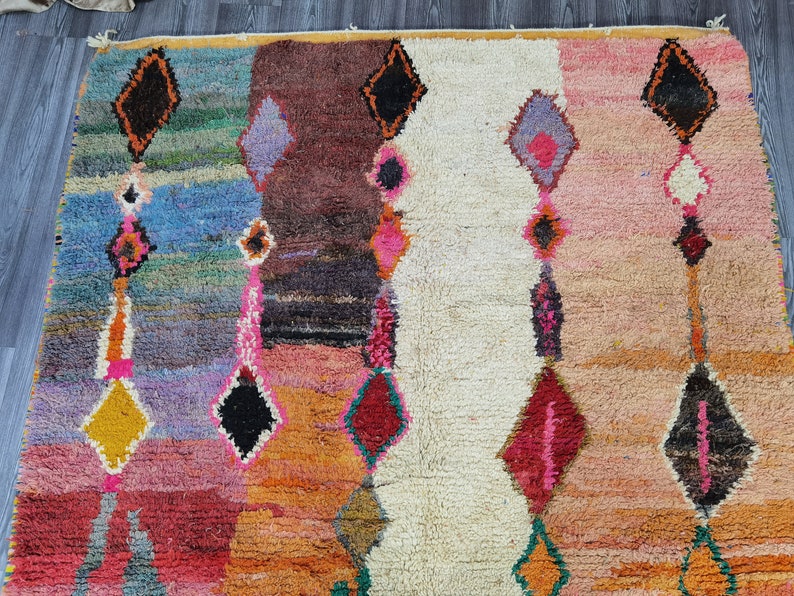 May include: A colorful Moroccan rug with a geometric pattern in shades of pink, orange, blue, and green. The rug has a white center section with a diamond pattern.