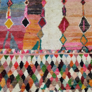 May include: A colorful Moroccan rug with a geometric pattern. The rug has a white background with a diamond pattern in shades of pink, red, orange, green, blue, and black.