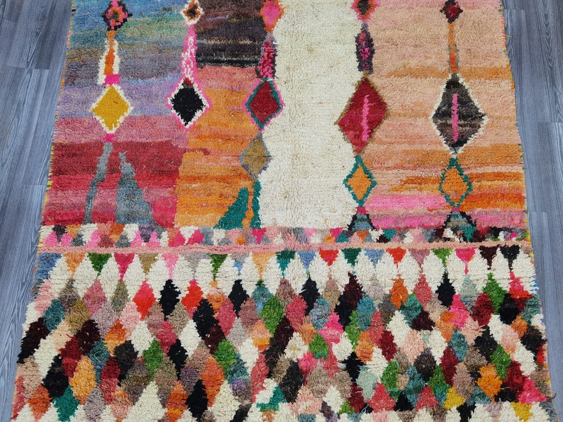 May include: A colorful Moroccan rug with a geometric pattern. The rug has a white background with a diamond pattern in shades of pink, red, orange, green, blue, and black.
