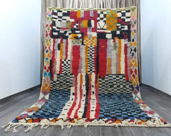 May include: A colorful Moroccan rug with geometric patterns in shades of red, blue, yellow, and black. The rug has a fringe border and is made of wool.