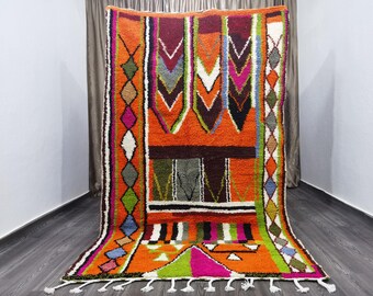 May include: A colorful Moroccan rug with geometric patterns in shades of orange, green, pink, blue, and white. The rug has a fringe border and is made of wool.