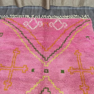 Op de afbeelding: Roze Marokkaanse tapijt met een geometrisch patroon met kruisen en zigzag in geel, oranje en groen.