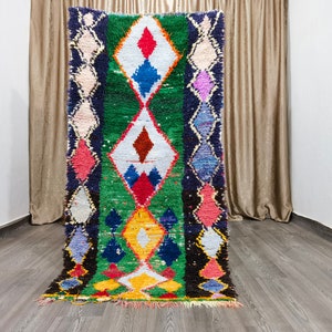May include: A colorful Moroccan rug with a geometric diamond pattern in shades of green, blue, red, yellow, and white. The rug has a fringe border.
