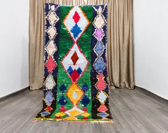 May include: A colorful Moroccan rug with a geometric diamond pattern in shades of green, blue, red, yellow, and white. The rug has a fringe border.