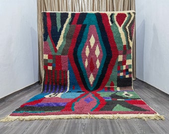 May include: A colorful Moroccan rug with a geometric pattern in shades of red, blue, green, and black. The rug has a fringe border and is woven with a variety of textures.