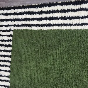 May include: A close-up of a textured rug with a green centre and a border of black and white stripes. The rug has a soft, plush appearance, suggesting a comfortable and decorative home textile.